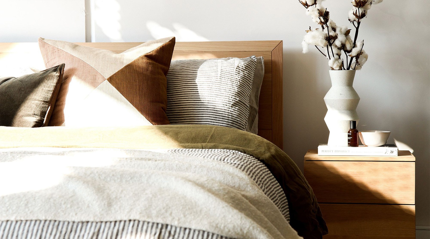 Sleep in style swath of sunlight shines across a well made bed and bedside table with a vase of cotton plants